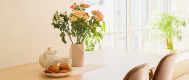 Mutfaktaki masasında güzel güller, çaydanlık, fincanlar ve kurabiyeler olan vazo