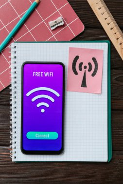 Ahşap zemin üzerinde WiFi sembolü olan kırtasiye malzemeleri ve cep telefonu.