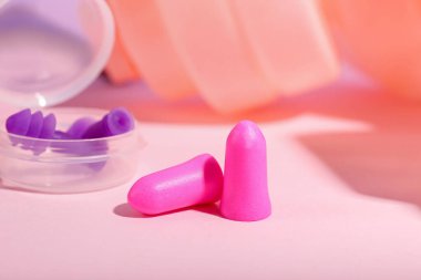 Pembe arka planda kulak tıkaçları olan plastik bir kap.