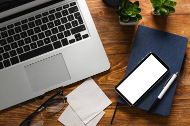 Cep telefonu, not defteri ve ahşap arka planda yapışkan notları olan bir laptop. Ticaret konsepti