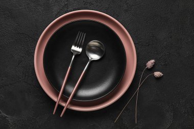 Siyah arka planda çatal bıçak ve çiçek dekoru olan tabaklar.