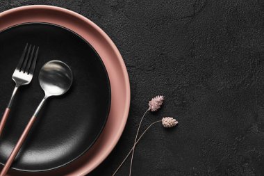 Siyah arka planda çatal bıçak ve çiçek dekoru olan tabaklar.