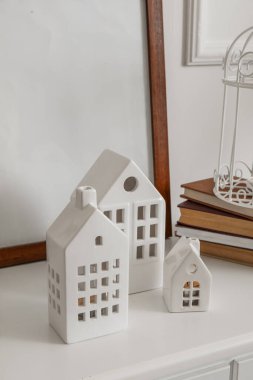 Ev şekilli mum tutucular, çerçeve ve kitaplar ışık duvarının yanındaki masada.