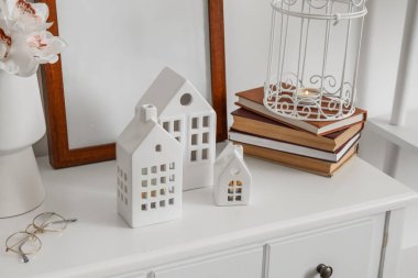 Ev şekilli mum tutucular, çerçeve ve kitaplar ışık duvarının yanındaki masada.