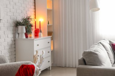 İçinde Noel dalları, vazolar, çekmeceler ve mumlar olan oturma odası.