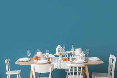 Mavi duvarın yanında mum tutacaklı ve mandalinalı Noel masası.