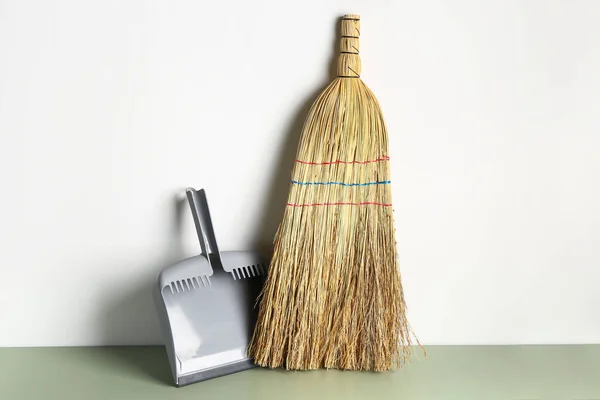 Cleaning broom and dustpan near light wall