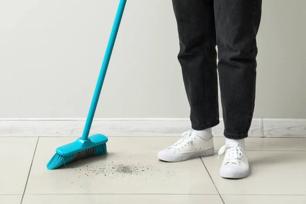Woman sweeping light tile floor with broom