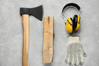 Yakacak odunları olan balta, işitme koruyucular ve grunge arka planda eldivenler.