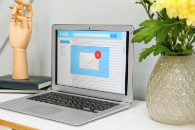 Gri duvarın yanındaki ışıklı masada açık e-posta kutusu olan modern dizüstü bilgisayar