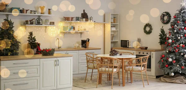 Interior of light kitchen with Christmas trees, shelves and dining table