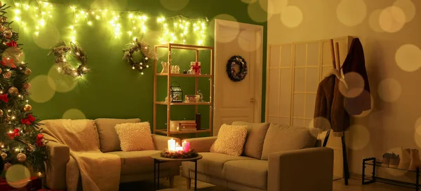 Interior of dark living room with Christmas tree, cozy furniture and glowing lights