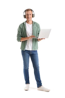 Kulaklık ve dizüstü bilgisayarı olan genç bir adam beyaz arka planda çalışıyor.