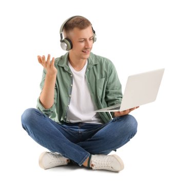 Kulaklık ve dizüstü bilgisayarı olan genç bir adam beyaz arka planda çalışıyor.