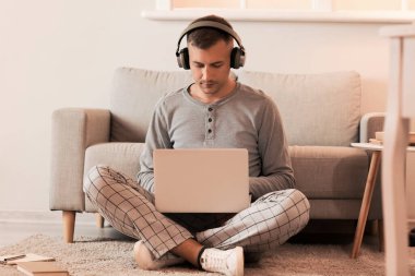 Kulaklık ve dizüstü bilgisayarı olan genç adam gece geç saatlerde evde ders çalışıyor.