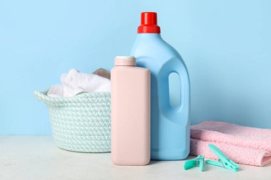 Çamaşır deterjanı, havlu ve sepet mavi arka planda.