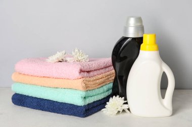 Çamaşır deterjanı ve güzel çiçekli havlular gri arka planda.