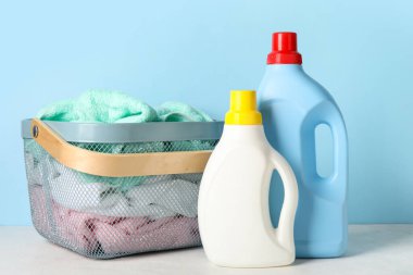 Çamaşır deterjanı ve sepette mavi arka planda giysiler var.