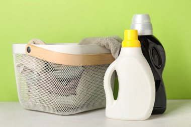 Çamaşır deterjanı ve sepette yeşil arka planda giysiler var.