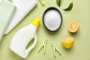 Yeşil arka planda çamaşır deterjanı, havlu ve limon.