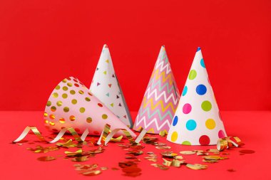 Kırmızı arka planda parti şapkaları ve konfetiler
