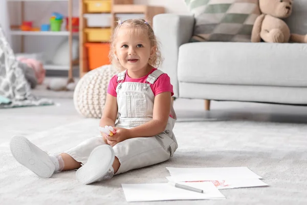 Cute little girl with felt-tip pens sitting on floor at home