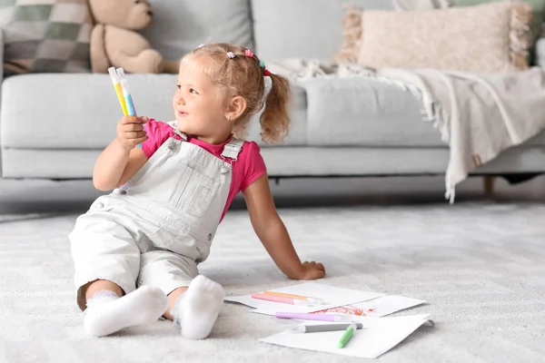 Cute little girl with felt-tip pens sitting on floor at home