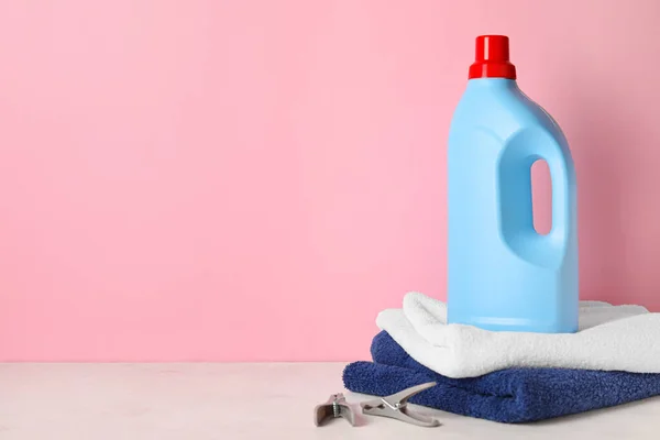 Laundry detergent and towels on table against pink background
