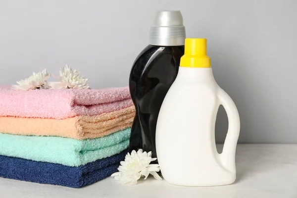 Laundry detergents and towels with beautiful flowers on table against grey background