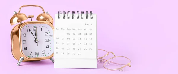 Flip calendar with alarm clock and eyeglasses on lilac background
