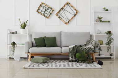 Gri kanepeli, raf üniteli ve çiçekli dağınık oturma odasının içi.