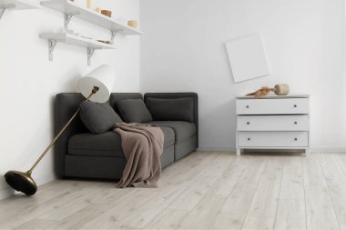 İçinde siyah kanepe, standart lamba ve çekmeceler olan dağınık bir oturma odası.