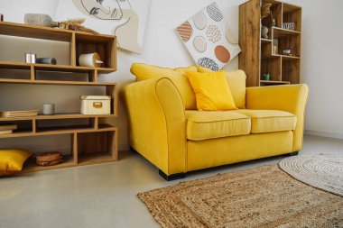 Oturma odasının iç tarafındaki beyaz duvarın yanında rahat bir kanepe ve ahşap raf ünitesi.