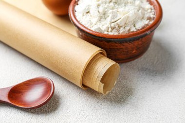 Bir rulo kağıt, un dolu bir kase ve arka planda tahta kaşık, yakın plan.