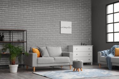 Gri tuğla duvarın yanında modern mobilyaları olan şık bir oturma odası.