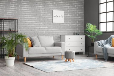 Gri tuğla duvarın yanında modern mobilyaları olan şık bir oturma odası.