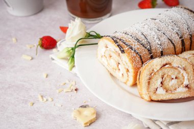 Lezzetli kek rulosu, taze çilek ve açık arkaplanda çiçek dekoru olan bir tabak.