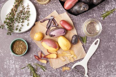 Soyulmuş çiğ patates, soyucu, otlar ve arkaplanda baharatlarla kompozisyon