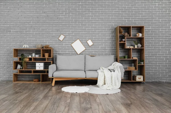 Interior of messy living room with sofa, shelf units and blank photo frames on grey brick wall