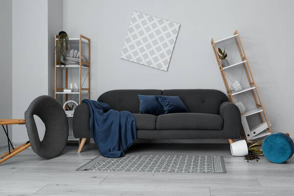 Interior of messy living room with shelf units and sofa near light wall