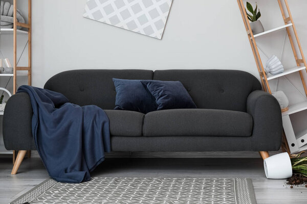 Sofa with plaid and pillows near light wall in messy living room