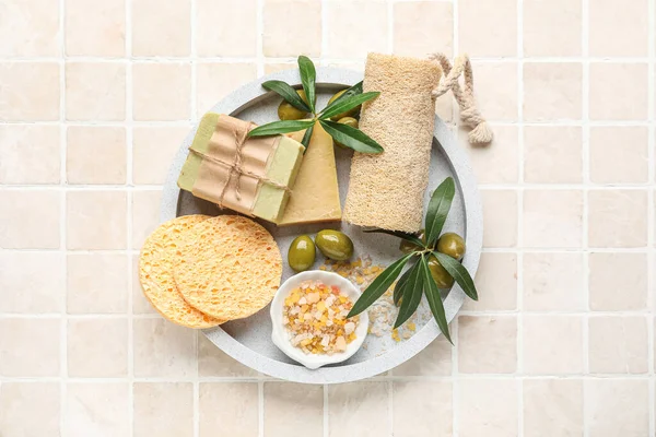 Board with soap bars, olives, sponges, sea salt and loofah on beige tile background