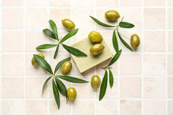 Soap bar with green olives and plant branches on beige tile background