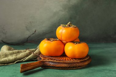 Wooden board with ripe persimmons on color table clipart