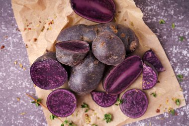 Çiğ mor patatesli bir yaprak kağıt ve arkaplanda baharatlar, yakın plan.