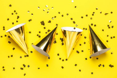 Sarı arka planda parti şapkaları ve konfeti