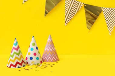 Sarı arka planda parti şapkaları, bayraklar ve konfetiler