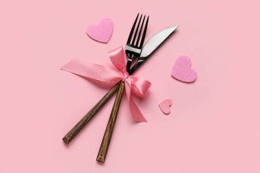 Sevgililer Günü için çatal bıçak seti. Pembe arka planda yay ve kalplerle.