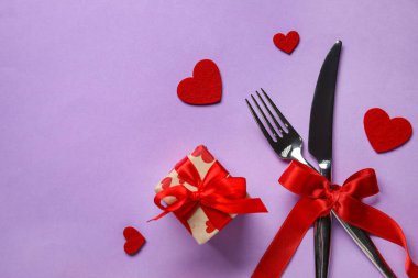 Sevgililer Günü için çatal bıçak seti, menekşe arka planda yay, hediye ve kalplerle