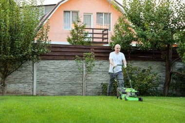 Arka bahçede çim biçme makinesiyle çim biçen genç bir adam.